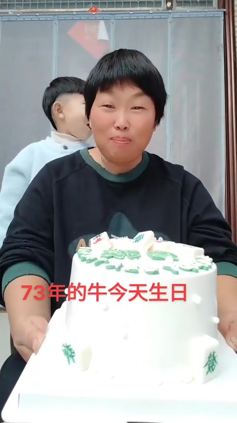 女士捧生日蛋糕，孩子在身后微笑